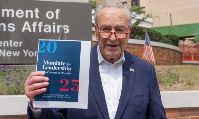 U. S. Senator Charles Schumer holds briefing in front of VA Hospital in New York on July 28, 2024 while holding photo illustrations on GOP 'Project 2025' plan as it will erode benefits for veterans. (Shutterstock)